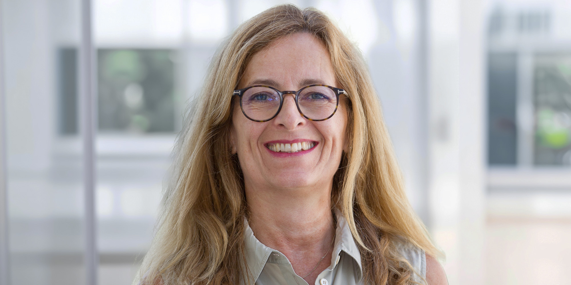 Marietta Lüders Marietta Lüders, lächelnd mit langen blonden Haaren und Brille, trägt eine helle Bluse vor einem hellen, unscharfen Hintergrund.