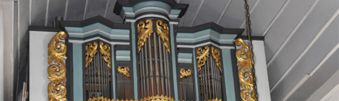 Mitarbeit an Kulturprojekten Detailansicht einer Kirchenorgel mit goldenen Verzierungen und Pfeifen vor einer hellgrauen Decke.